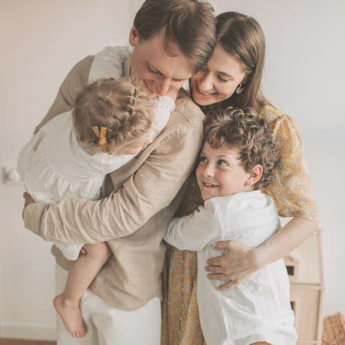 Familie (Mutter, Vater, Sohn, Tochter) kuscheln fröhlich